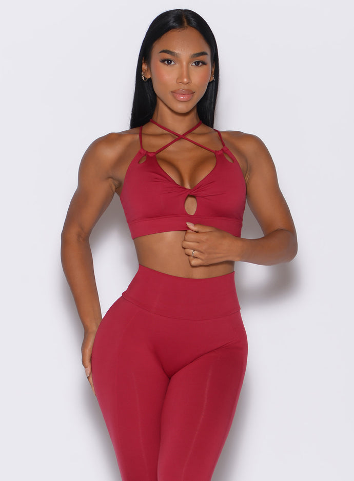 Front profile view of a model wearing our twist sports bra in maroon color along with a matching leggings 