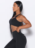 left side profile view of our model adjusting the waistband of the leggings wearing the Two Way Bra in Black color