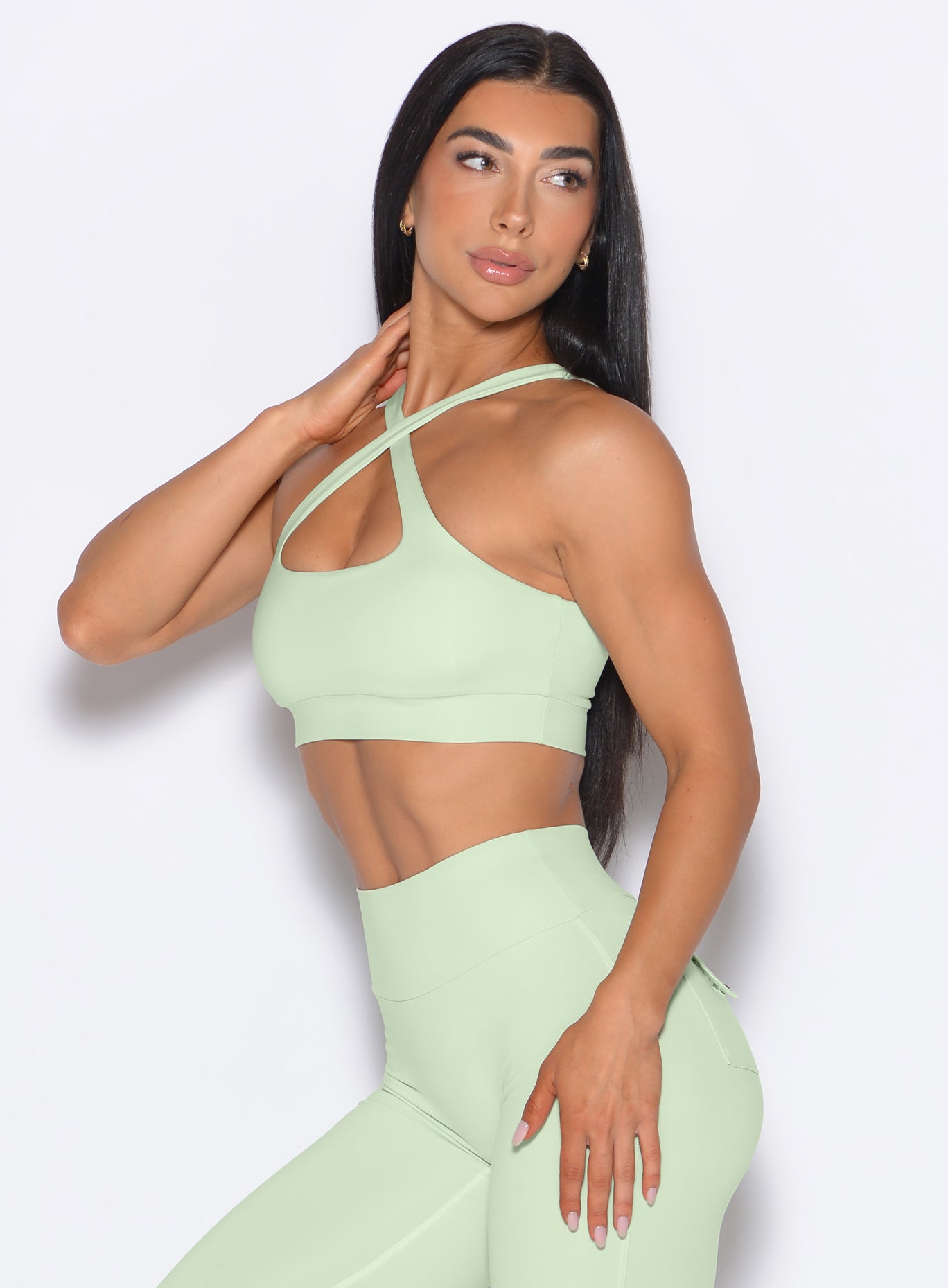 left side view of a model facing to her left wearing our Two Way Bra in Cool Matcha color and a matching leggings 
