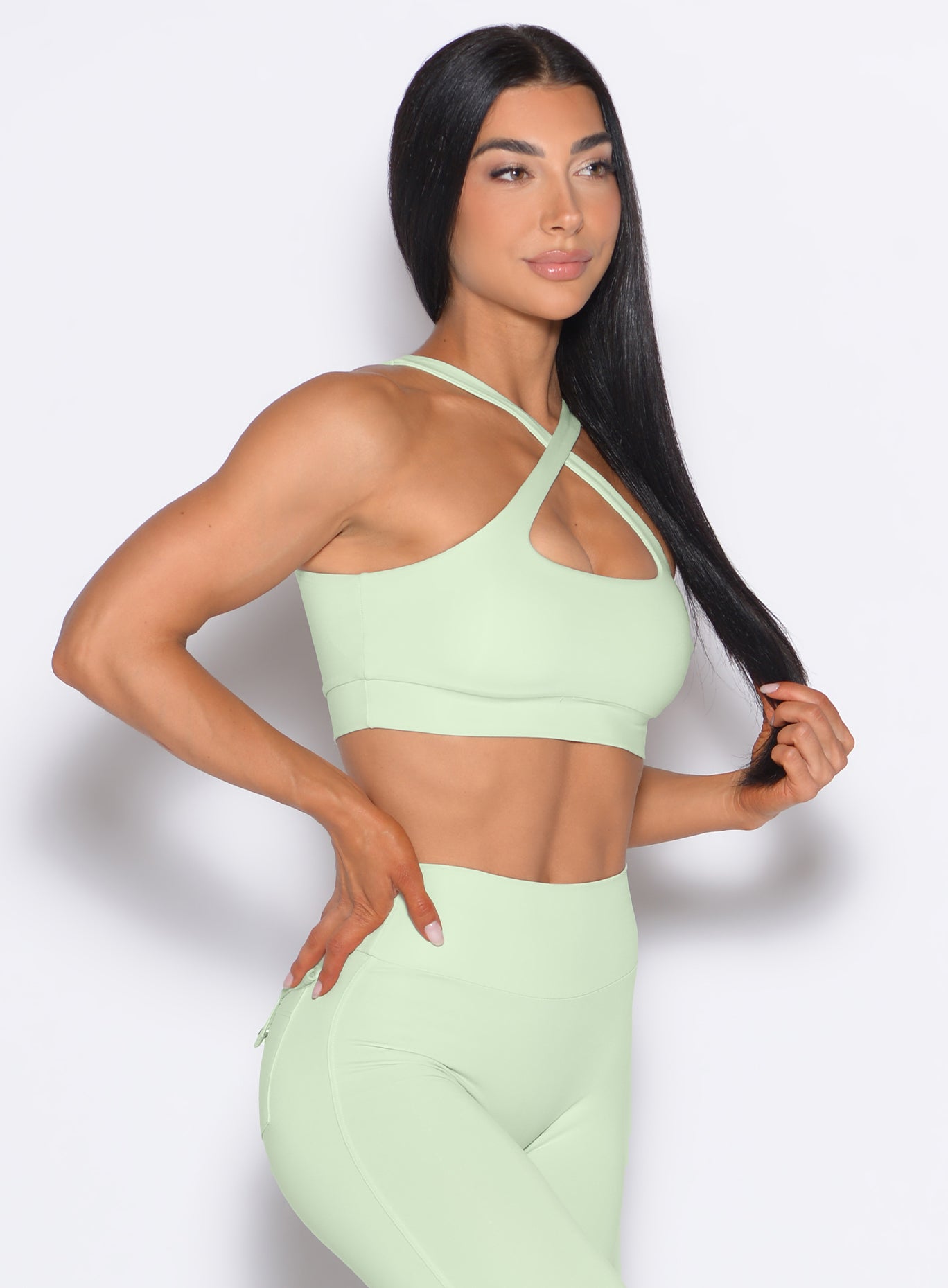 front profile view of a model posing in our Two Way Bra in Cool Matcha color and a matching leggings 
