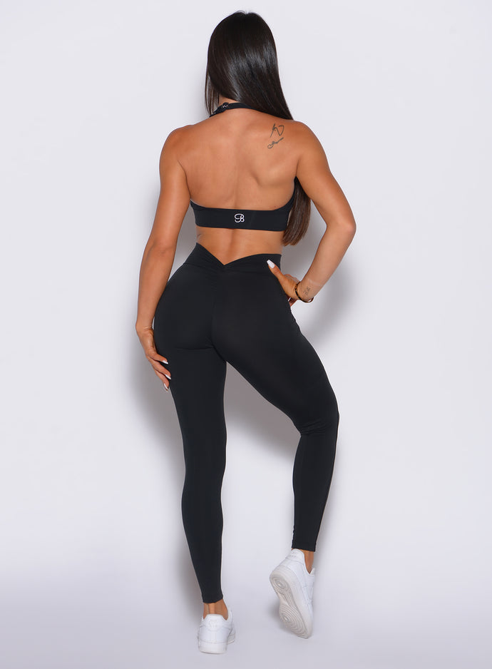 Back profile picture of a model wearing our black V back leggings and the matching bra  with her hand on her hip