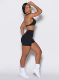 right side profile view of a model facing to her right  wearing our black V back shorts along with the matching sports bra