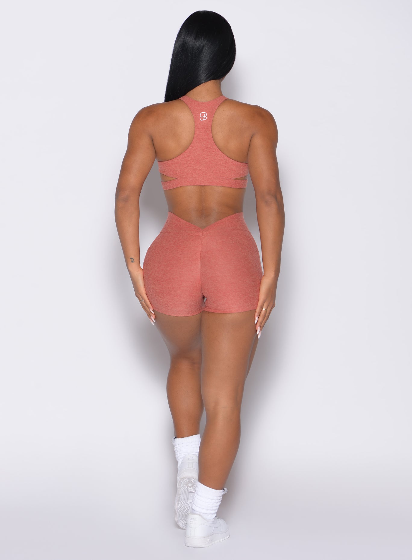 back profile view of a model with both hands on her thighs wearing the V Back Shorts in Georgia Peach color