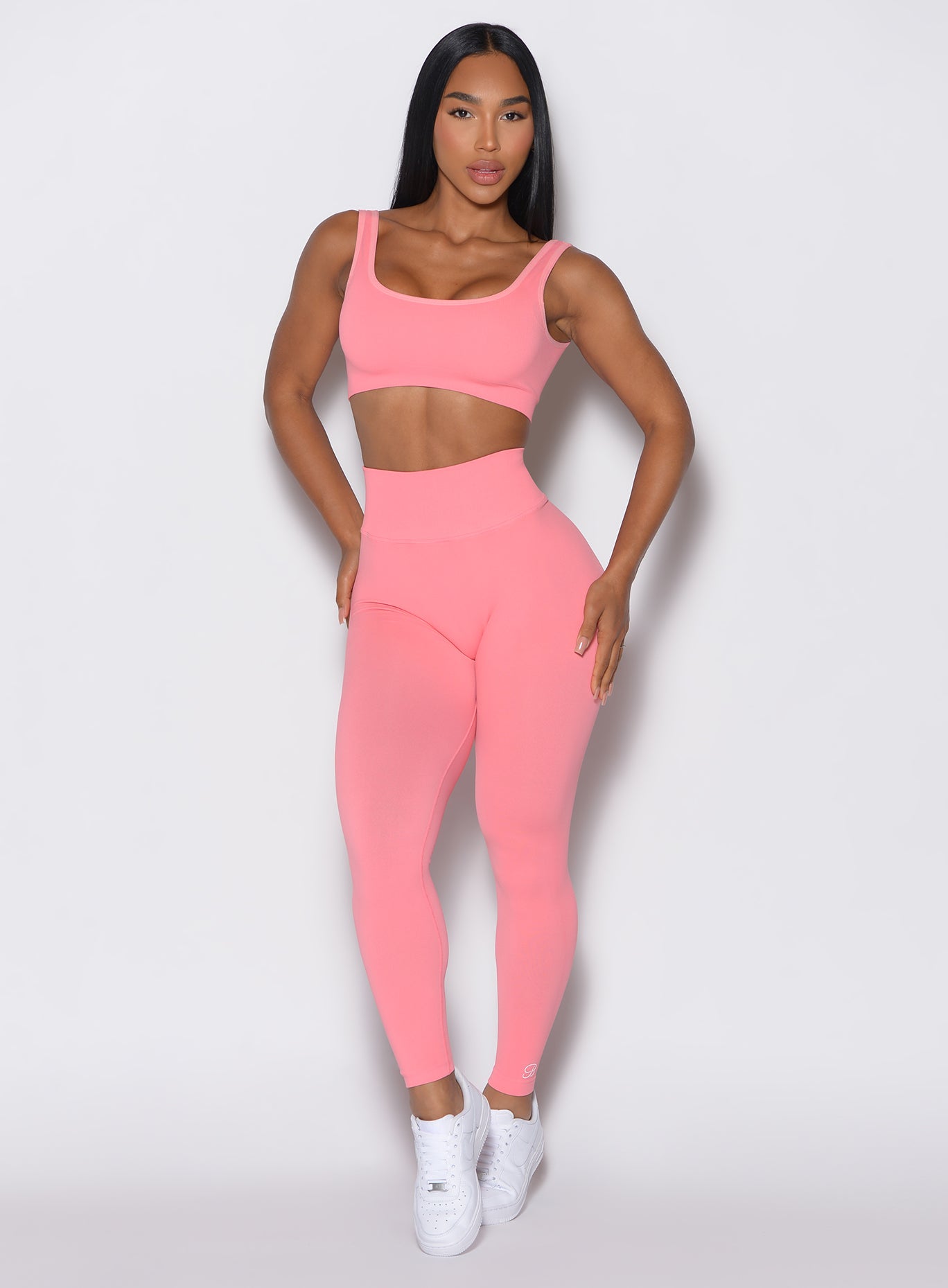 front profile view of a model facing forward wearing our v seamless leggings in flamingo color  along a matching sports bra