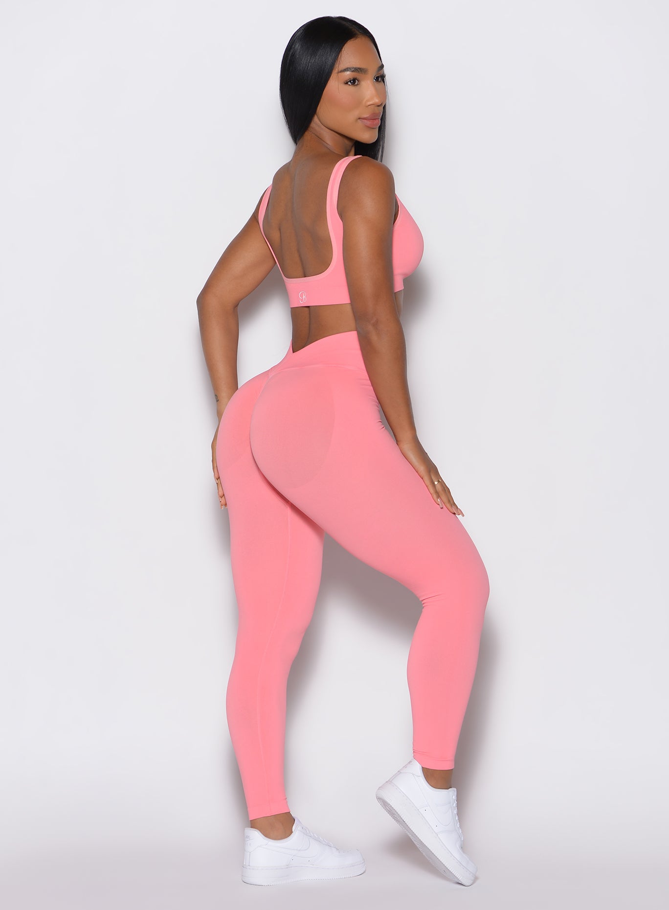 right side profile view of a model facing to her right wearing our v seamless leggings in flamingo color along a matching sports bra 