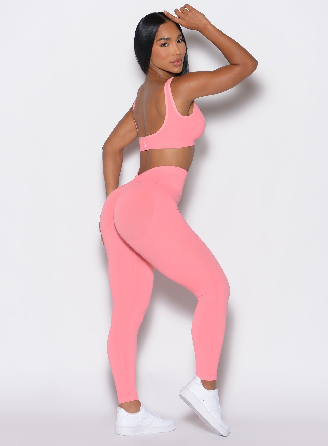 right side profile view of a model facing to her right wearing our v seamless leggings in flamingo color  along a matching sports bra