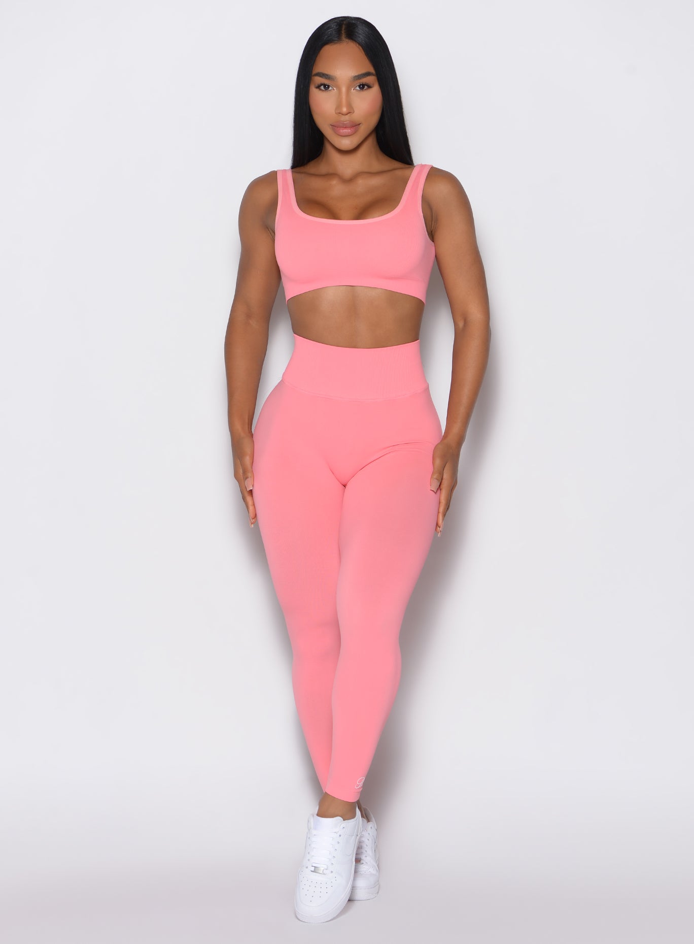 front profile view of a model facing forward wearing our v seamless leggings in flamingo color along a matching sports bra
