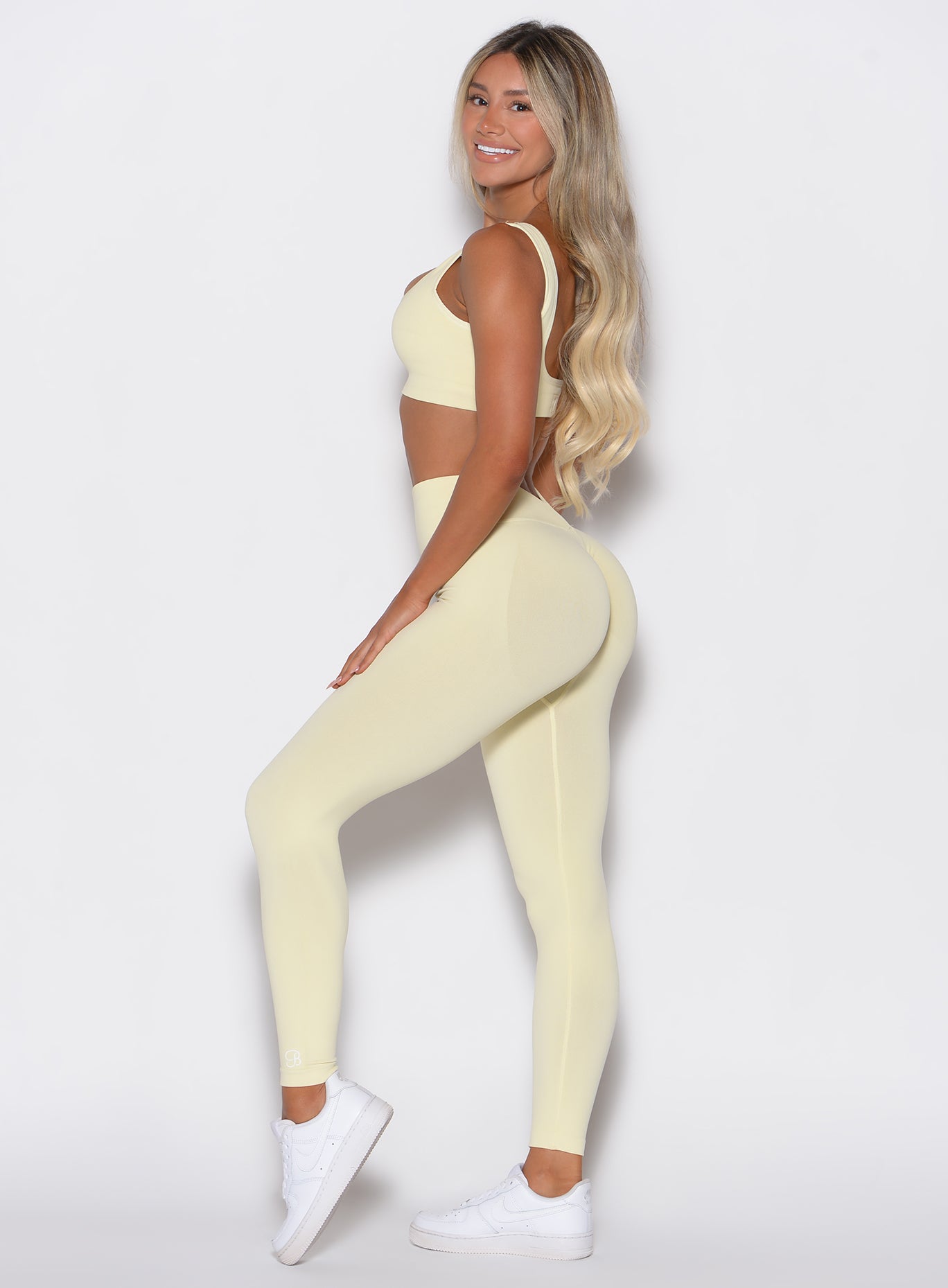 left side profile view of a model wearing our V Seamless leggings in Mellow Yellow, complemented with the matching sports bra
