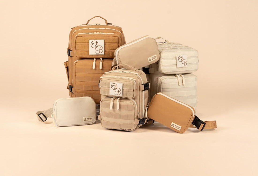 Stack of various backpacks and cross body bags in cream, light brown, and camel colored. Each bag features a WOLFpak and Bombshell logo patch