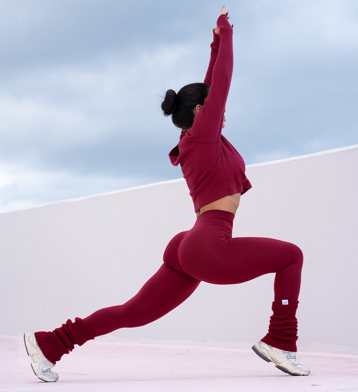 Model stretching legs and arms while wearing red internal scrunch leggings, allure long sleeve and luxe leg warmers