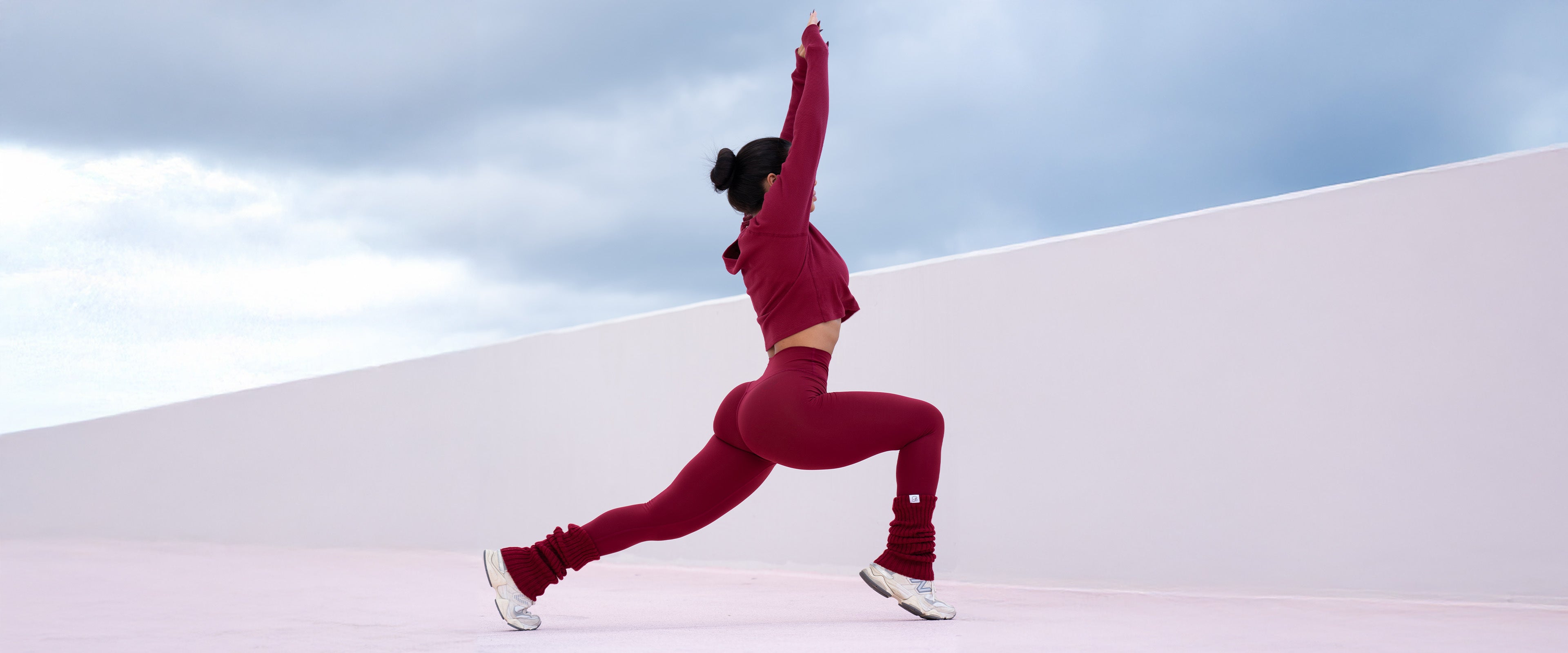 Model stretching legs and arms while wearing red internal scrunch leggings, allure long sleeve and luxe leg warmers