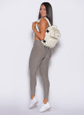 left side profile view of our model carrying a backpack wearing the Bombshell Bunny Leggings in smoked taupe color