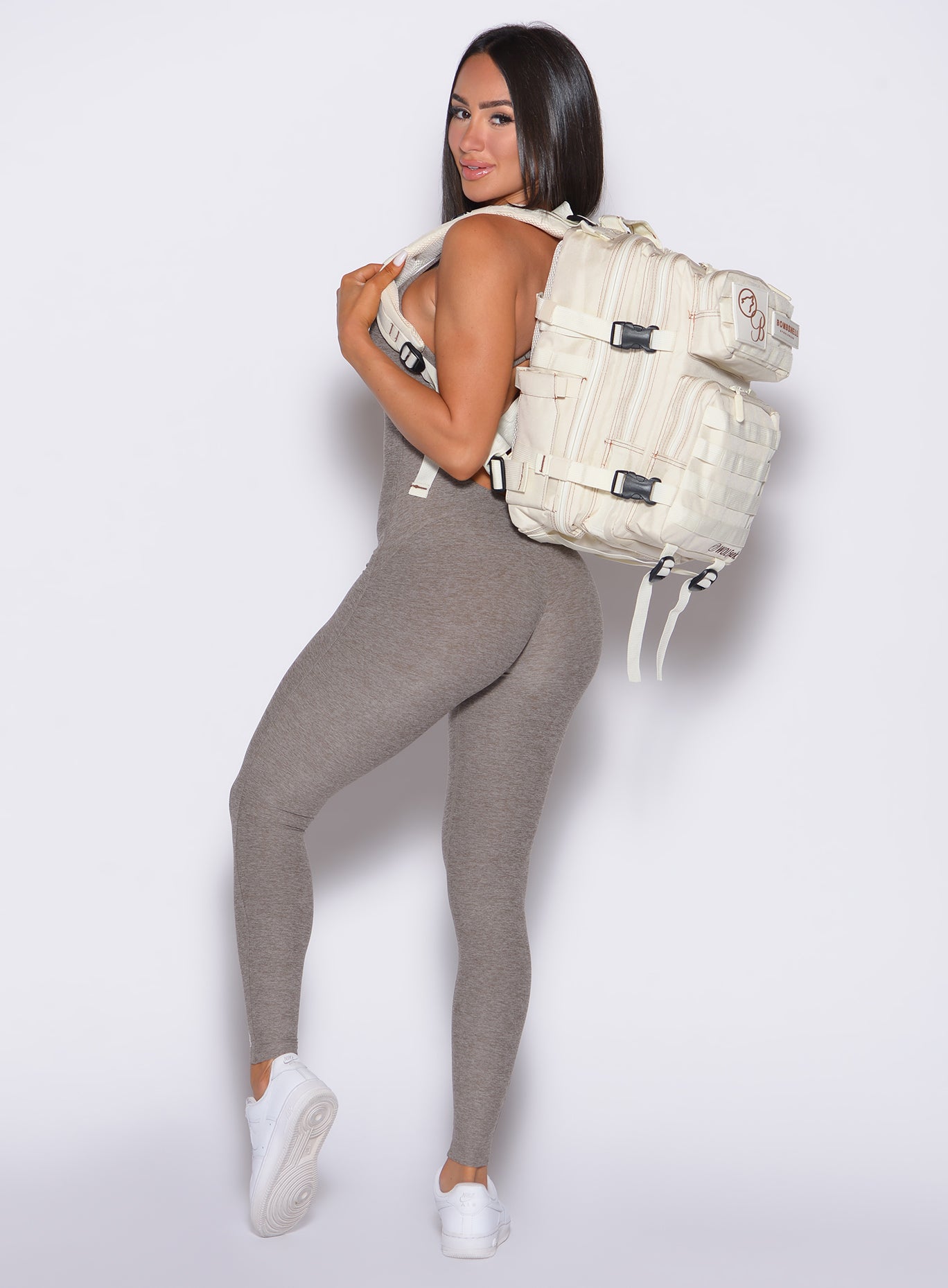 left side profile view of our model wearing the Bombshell Bunny Bodysuit 2.0 in Smoked Taupe color equipped with the Bombshell X WOLFpak collaboration backpack. 