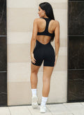 Back profile view of a model facing to her right wearing our black zip bodysuit shorts