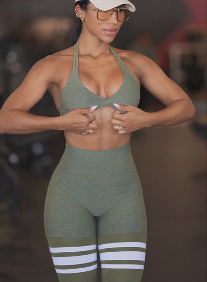 A short video of a model wearing our Scrunch Thigh-Highs and matching bra in Lily Pad color, paired with a white hat and glasses, working out in a gym