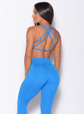 Back profile view of a model wearing our barbell sports bra in crystal pop blue color and a matching leggings