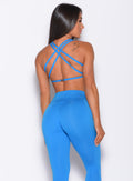 Back profile view of a model in our barbell sports bra in crystal pop blue color and a matching leggings