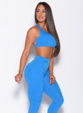 Right side profile view of a model in our barbell sports bra in crystal pop blue color and a matching leggings