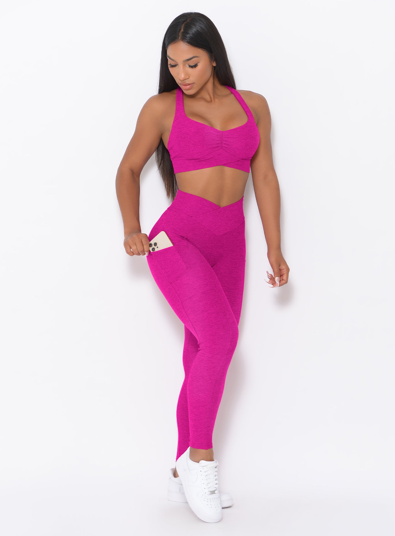 Model facing forward taking out the phone from her pocket wearing our Contour Leggings in Ultra Pink color and a matching bra