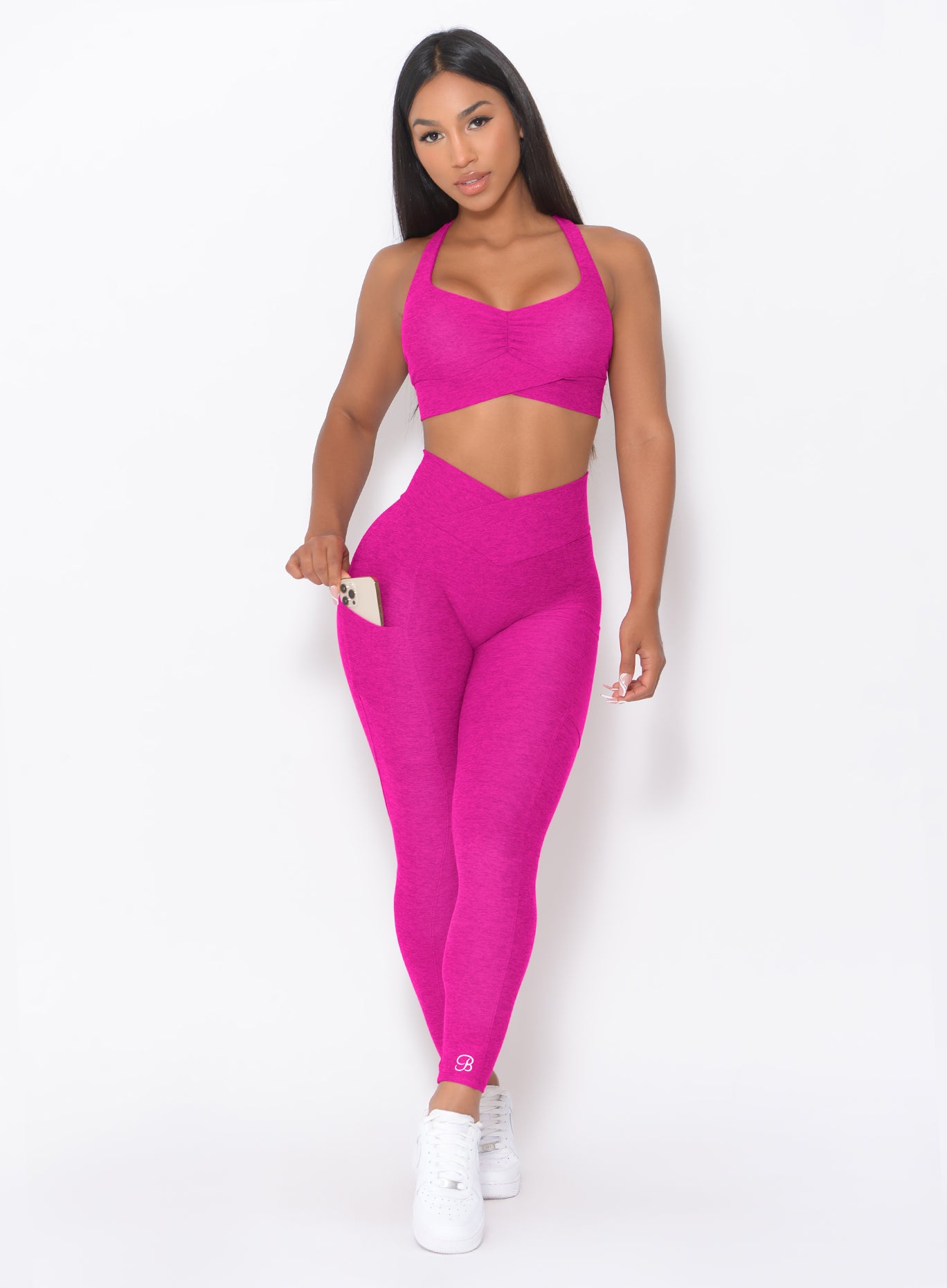 front profile picture of a model in our Contour Leggings in Ultra Pink color and a matching bra holding her phone in the right pocket of the leggings