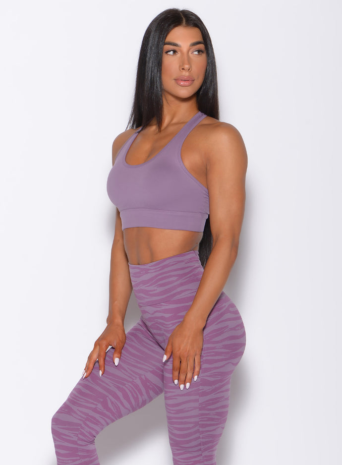 Left side profile view of a model angled slightly to her left wearing our rival sports bra in solid orchid color and a matching sexy back leggings in tiger print color 