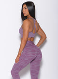 Left side profile view of a model in our rival sports bra in solid orchid color and a matching sexy back leggings in tiger print 