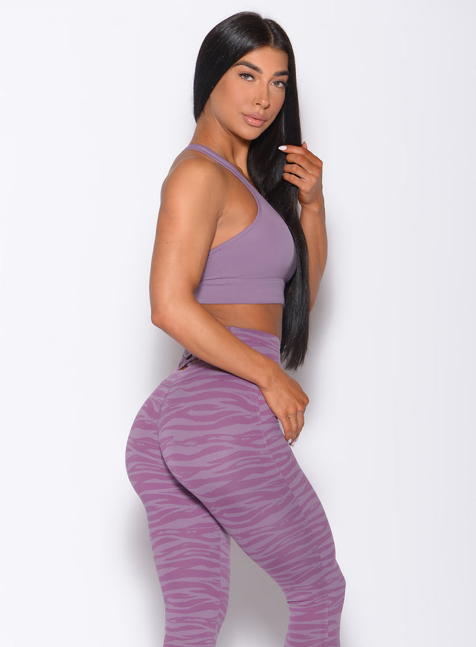 Right side  profile view of a model in our rival sports bra in solid orchid color and a matching sexy back leggings in tiger print