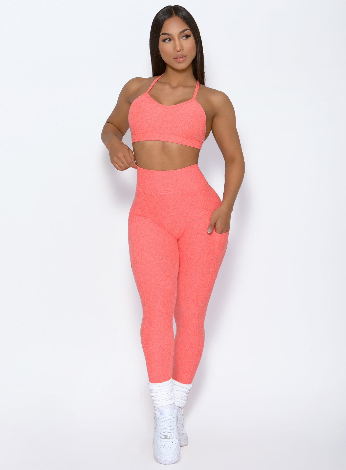 front profile view of a model wearing Curve leggings and the Braid Back Sports Bra in Coral color