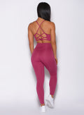 Back profile view of a model wearing our empower leggings in berry good color and a matching bra