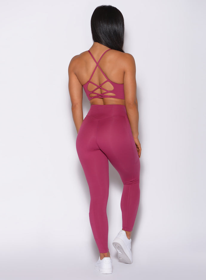 Back profile view of a model wearing our empower leggings in berry good color and a matching bra