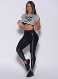 Front profile view of a model wearing our gloss black leggings and a gray tee 