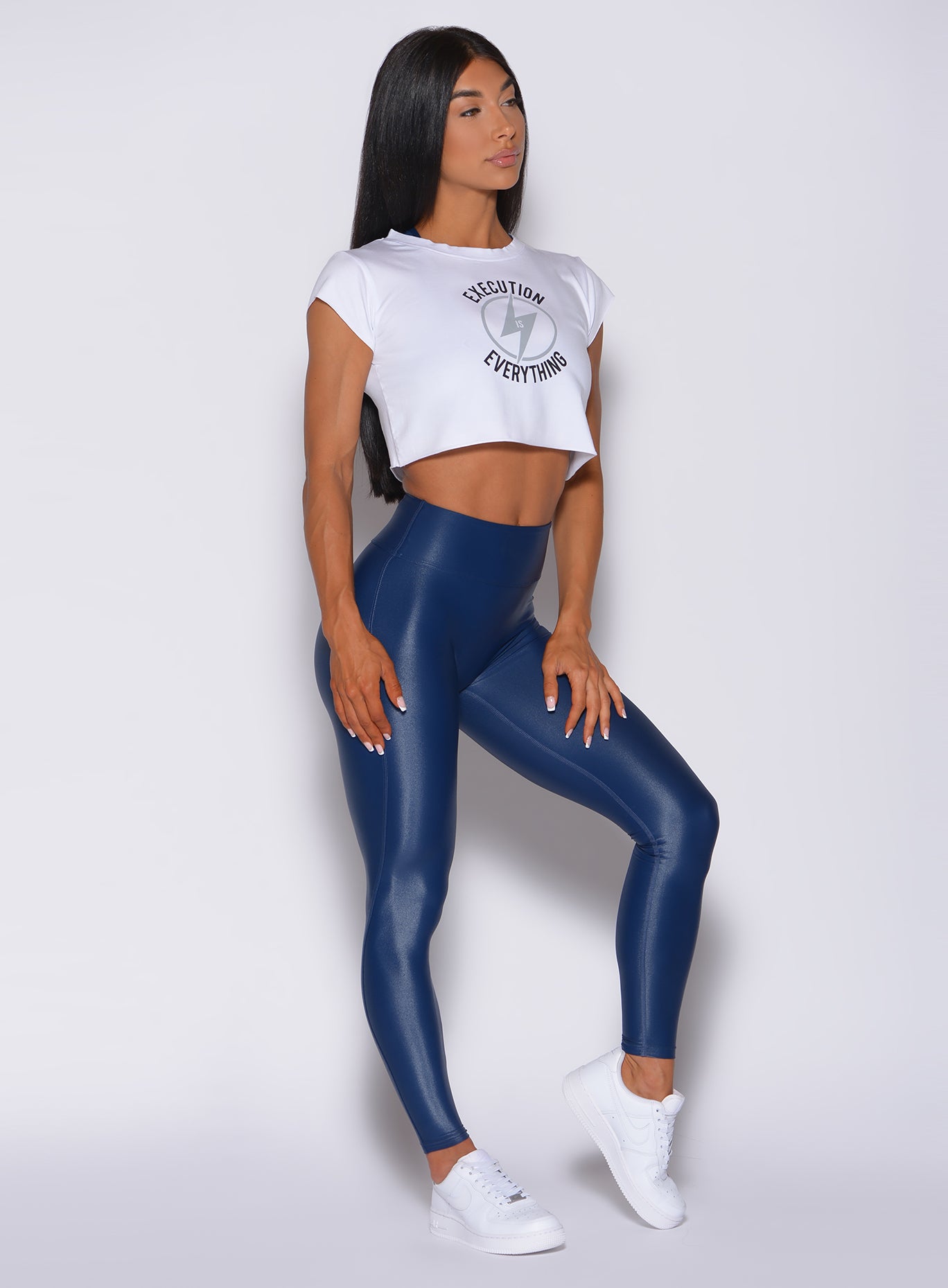 Right side profile view of a model wearing the white execution tee and a navy gloss leggings