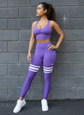 front view of the model with her hand on hip wearing our perform thigh highs in royal purple color with three white stripes on thighs and a matching bra