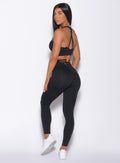 Left side profile view of a model facing to her left wearing our black sexy back leggings and a matching bra 